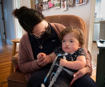 A woman holds a young child with medical tubes.