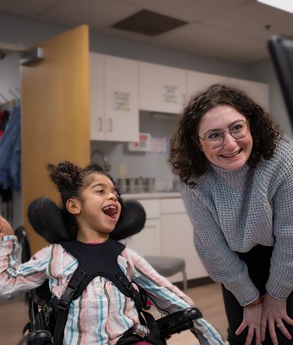 Girl in wheelchair smiling with woman.