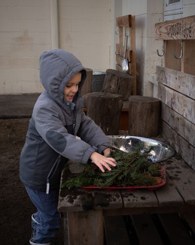 Child in winter coat playing with branches.