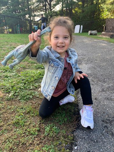 Young girl holding a toy dinosaur.